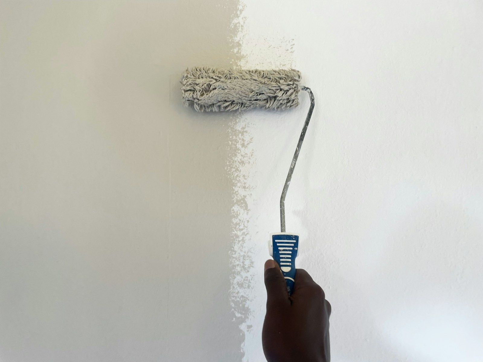 Paint roller applying a fresh coat of white paint to a wall